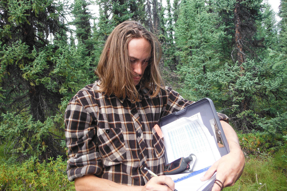 Cam in the forest writing observations on a clipboard