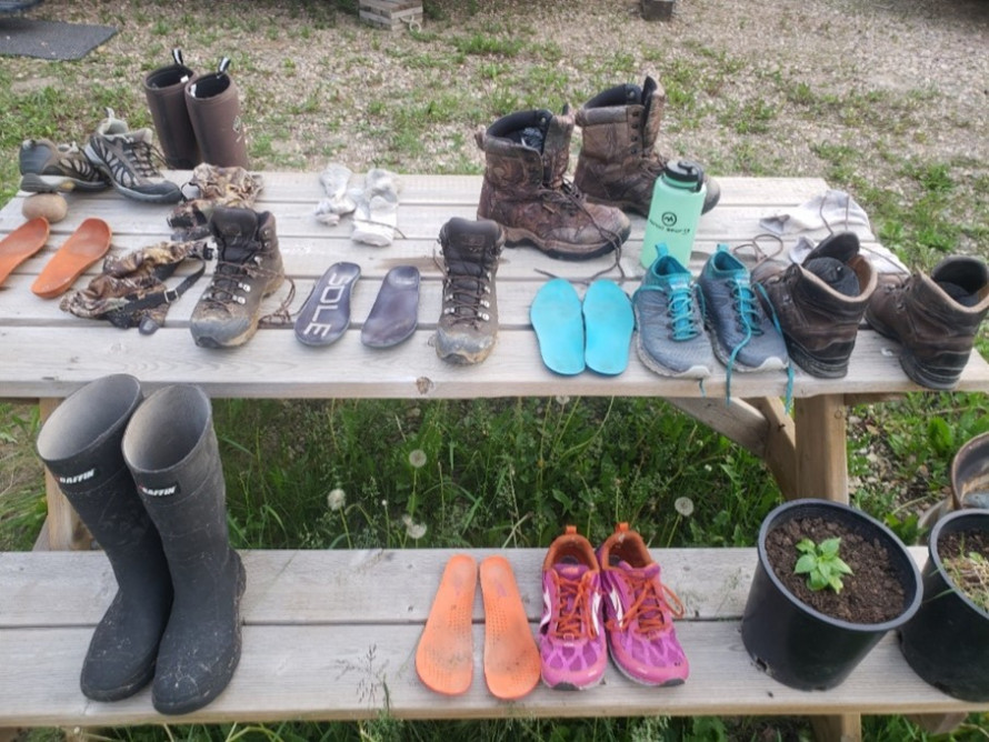 Many pairs of boots, shoes, and flip flops drying on a picnic table