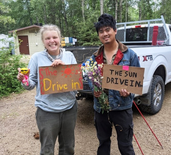 Janine and Christian with cardboard signs that say The Sun Drive In.