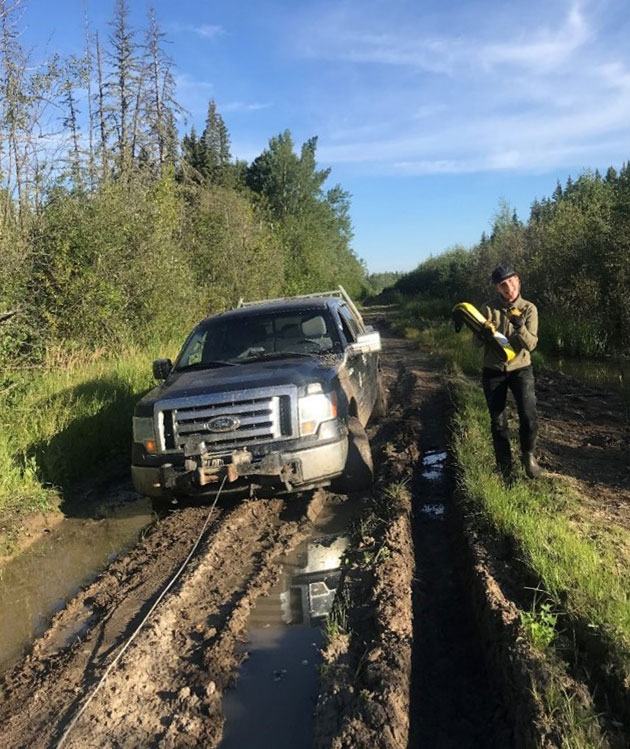 pickup truck stuck in muddy ruts. winch cable played out. smiling field tech standing nearby