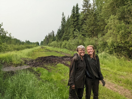 2 field technicians covered in mud, on a grassy road in the Chinchaga