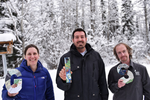 3 GIS employees stand outside in the winter holding wooden block letters spelling GIS