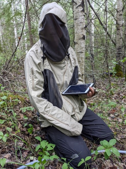 Field technician sitting in the grass in a bug jacket