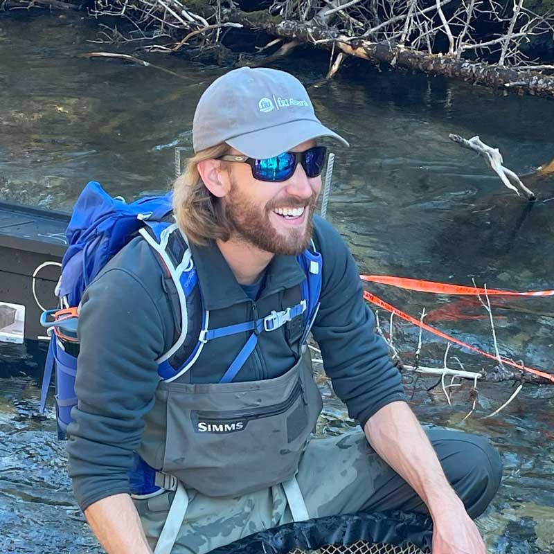 Dr. Benjamin Kissinger holding kneeling in a stream with field equipment