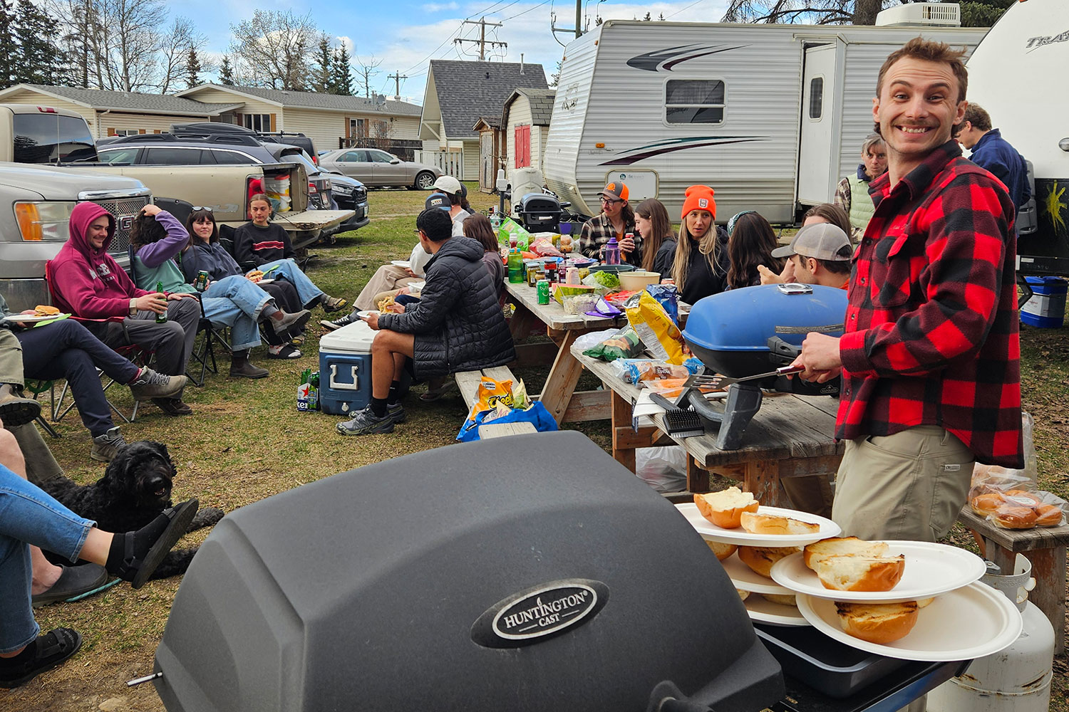 A group of people sit on picnic benches and folding chairs eating BBQ