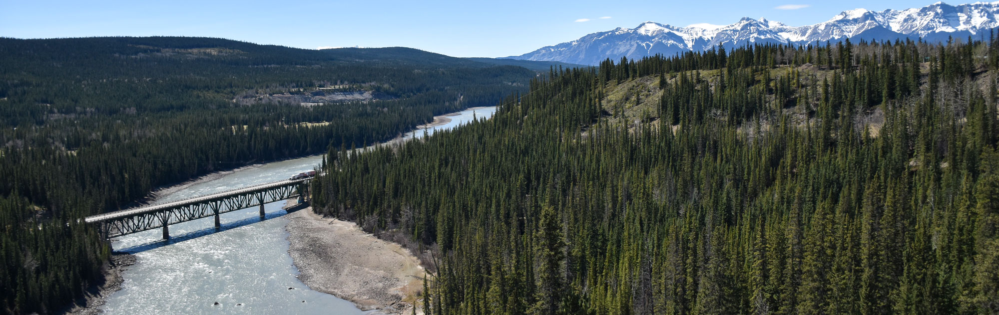 a bridge over the athabasca river in the foothills with mountains in the background