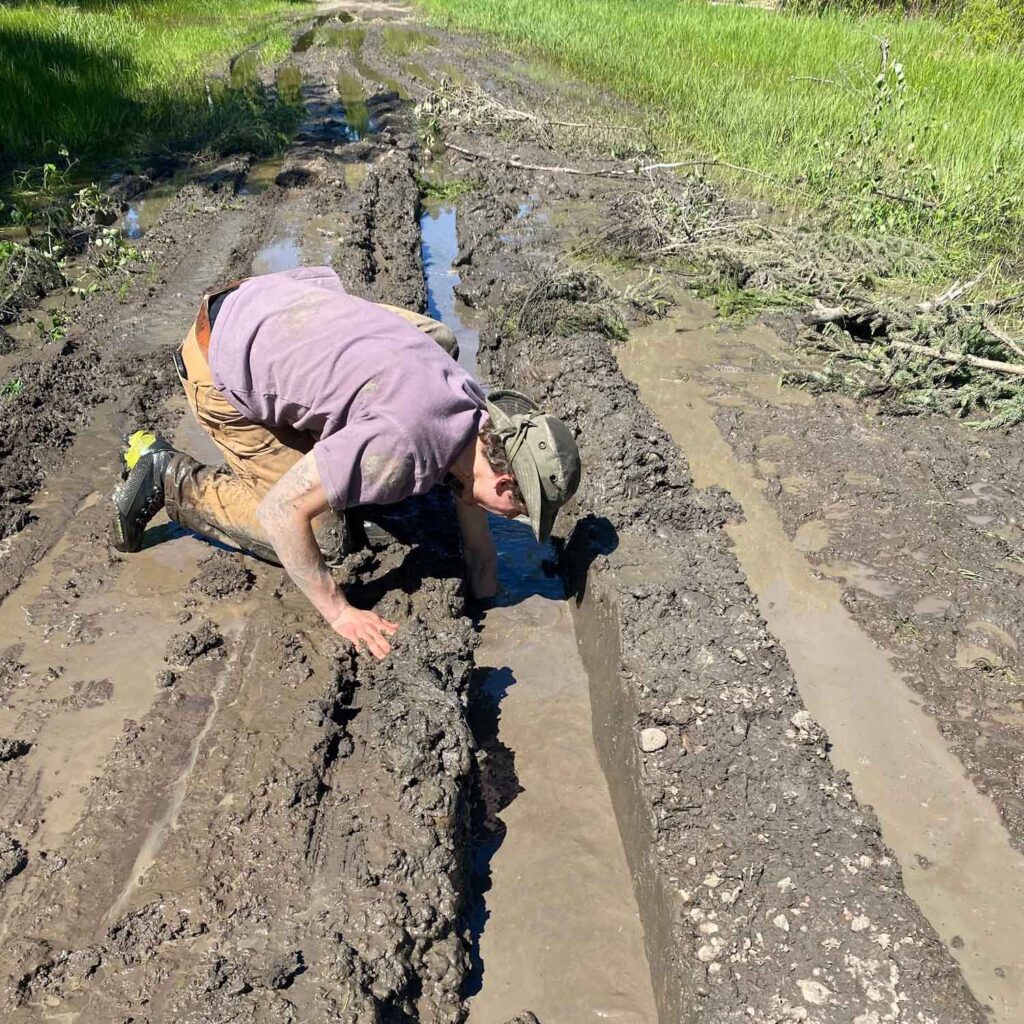 darko gojsic kneeling on a muddy road reaching down past his elbow into a mud puddle trying to retrieve a skidplate