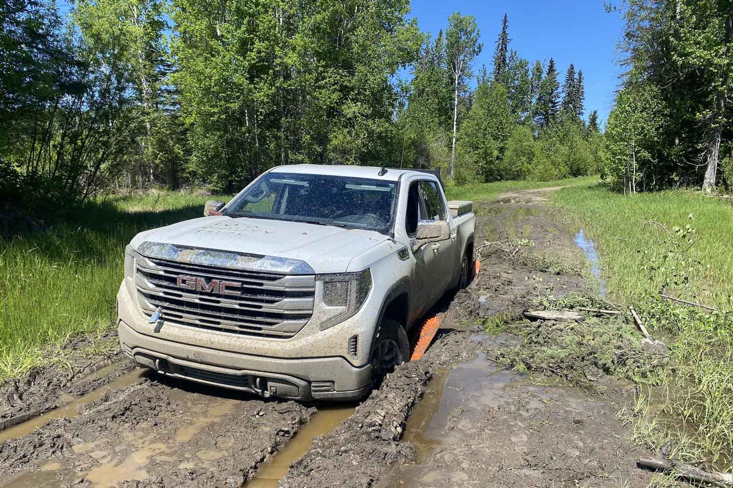 a white pickup truck stuck in deep mud, burried skidplates under the tires