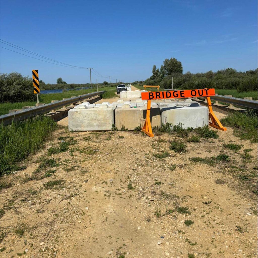 a bridge is blocked off by large concrete barriers and an orange bridge out sign. a truck is parked on the far side photo: javier puac