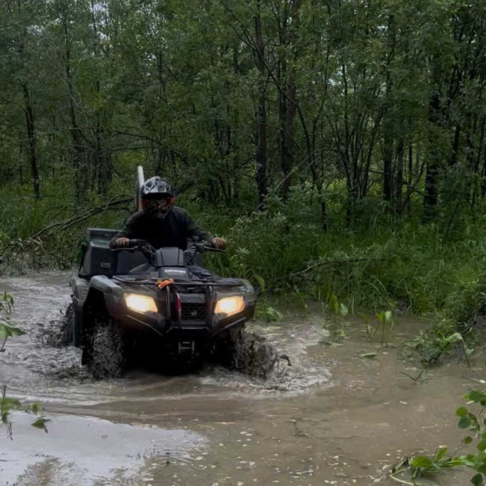 an atv rider in helmet drives down a flooded road with over a foot of standing water. photo: landon bick