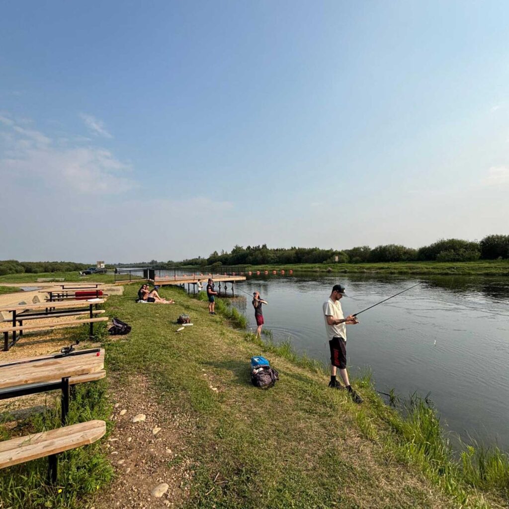 members of the crew sit on a bank or stand at the river's edge fishing. there are picnic tables and a water deck. photo: javier puac