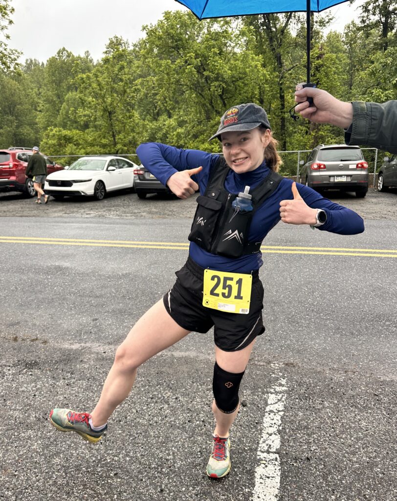 Brianna Lyman stands in the parking lot before doing the Charlie Half Marathon Trail Race. She holds two thumbs up and is smiling.