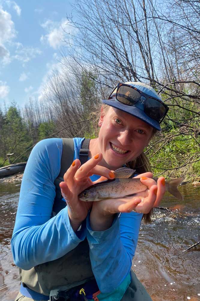 hailey holds an arctic grayling in a stream. 
